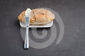 Croissant and a knife with butter on a dark stone table. Top view, copyspace. French breakfast