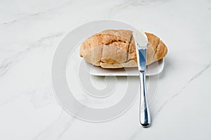 Croissant and a knife with butter on a white stone table. French breakfast