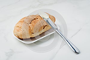 Croissant and a knife with butter on a white stone table. French breakfast