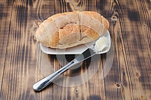 Croissant and a knife with butter on a wooden table. French breakfast