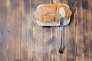 Croissant and a knife with butter on a wooden table.Top view, copyspace. French breakfast