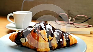 Croissant with Moist Chocolate Sauce and a Cup of Steaming Hot Coffee in Background