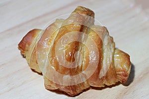 The croissant is placed on the wooden floor. It is a French crescent shaped roll made of sweet flaky pastry