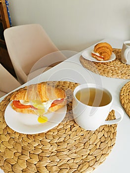 Croissant with poached egg and tomatoes with tea in the kitchen. Delicious breakfast in the white kitchen.