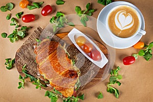 Croissant sandwich with cherry tomatoes and hot cappuccino coffee