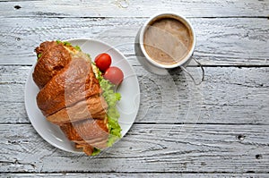 Croissant sandwich with chicken breast and lettuce. Croissant sandwich and coffee on a wooden table. Delicious