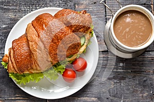 Croissant sandwich with chicken breast and lettuce. Croissant sandwich and coffee on a wooden table. Delicious