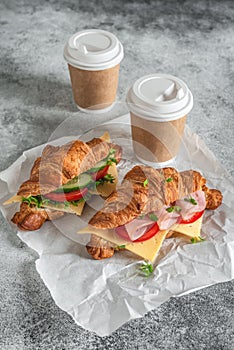 Croissant sandwich and cup coffee on gray concrete background. Croissants with ham and fresh vegetables. Side view, selective