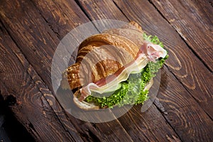 Croissant sandwich with jamon, cheese, fresh cucumbers and green salad leaves on rustic wooden table, closeup