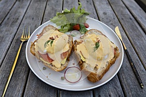 Croissant sandwich with poached egg, radish and salmon on plate in cafe