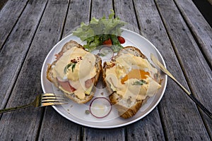 Croissant sandwich with poached egg, radish and salmon on plate in cafe