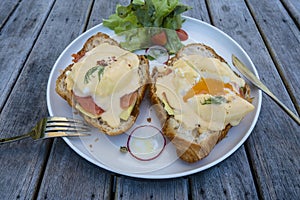 Croissant sandwich with poached egg, radish and salmon on plate in cafe