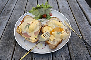 Croissant sandwich with poached egg, radish and salmon on plate in cafe