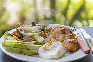 Croissant sandwich with poached egg, tomato and avocado on plate