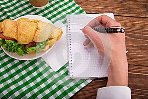 Croissant sandwich on a saucer. In the hands of a pen writes a b