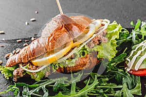 Croissant sandwich with tuna, avocado, fresh arugula and greens on black shale board over black stone background