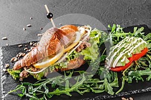 Croissant sandwich with tuna, avocado, fresh arugula and greens on black shale board over black stone background. Healthy food