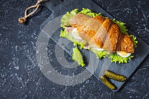Croissant sandwich with tuna, hard boiled egg, salad and cucumber on stone table