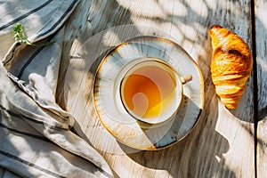 Croissant and teacup on a wooden table bathed in sunlight