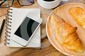 Croissants coffee notebook and smart phone on the wooden table - tone vintage.