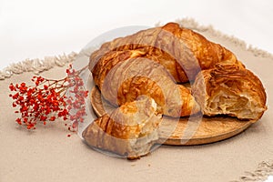 Croissants lie on a wooden textured plate on a jute textured napkin. French traditions