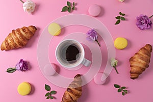 croissants and macarons with flowers and cup of coffee on pink background