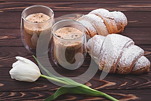 Croissants and two glasses of frothy coffee on a dark brown wooden table. French breakfast concept, break. Drinks and sweets, puff