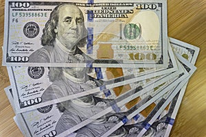 Crolled stack of 100 new dollar bills on wooden background