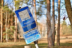 Crooked blue sign with German text `Water protection area` and English translation underneath