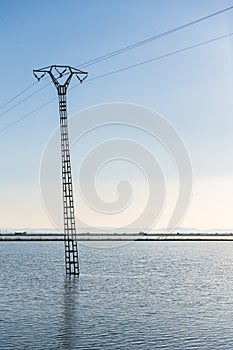 Crooked electrical pylon located in the middle of a flooded rice field