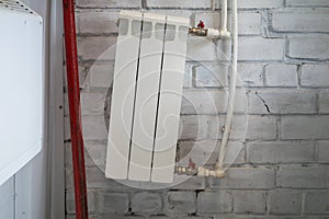 a crookedly installed white heating radiator of three sections on a brick wall background
