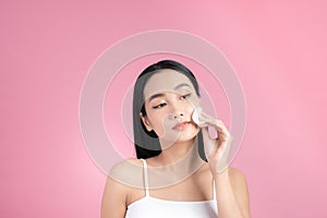 Crop attractive young female cleansing face with a cotton pad on a pink background in studio