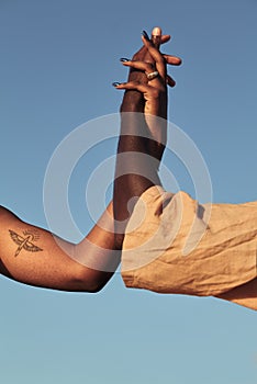 Crop black couple joining hands against blue sky