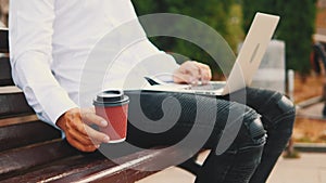 Crop. Businessman, wearing business style and typing on the laptop computer while sitting outdoors in the park on the