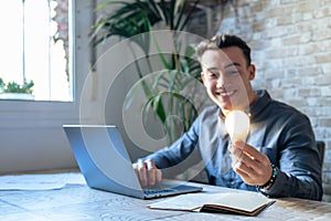 Crop close up of male employee work on computer hold bright light bulb get brilliant business idea. Businessman or worker feel