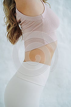 Crop close up photo of young woman in sportswear doing stretching on background of white wall