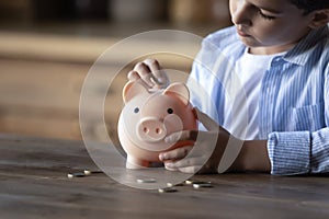 Crop close up 8s boy putting coin into piggy bank