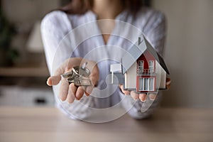 Crop close up woman realtor holding keys and house model