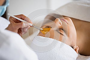 Crop cosmetologist with client during exfoliation procedure in spa salon