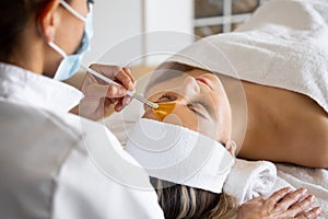 Crop cosmetologist with client during exfoliation procedure in spa salon