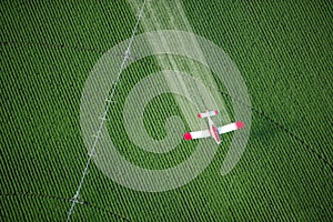 A crop duster spraying a green farm field.