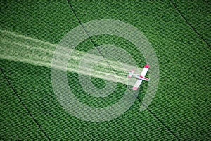 A crop duster spraying a green farm field.