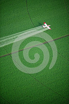 A crop duster spraying a green farm field.