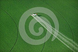 A crop duster spraying a green farm field.