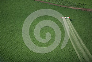 A crop duster spraying a green farm field.