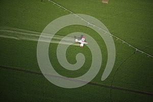 A crop duster spraying a green farm field.