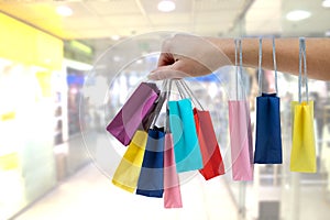 Crop female hand holding colorful paper bags on background of shopping center.