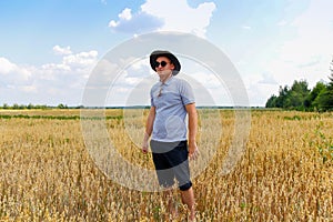 Crop and harvest. Portrait of farmer standing in gold wheat field with blue sky in background. Young man wearing