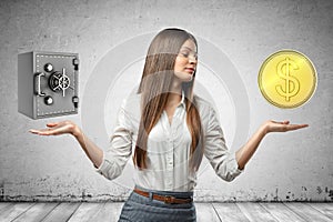 Crop image of young attractive businesswoman, hands at sides, levitating locked money vault and huge golden coin.