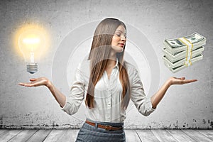 Crop image of young beautiful businesswoman, hands at sides, palms facing up and levitating lightbulb and stack of cash.